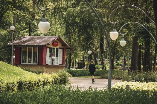 A tranquil park scene with lush greenery, people strolling, and vintage streetlights.