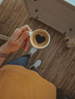 Overhead shot of a coffee cup with heart-shaped foam held by a person in a cozy setting.. pexels, overhead, shot