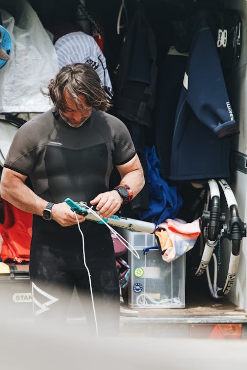 A man in a wet suit is looking at his surfboard