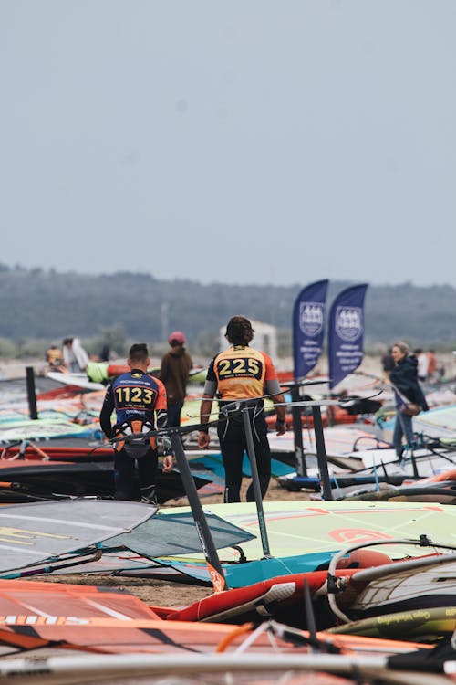 A group of people standing on the beach with windsurfers