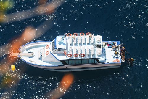 Free Aerial photo of a white boat with divers preparing to plunge into blue waters. Stock Photo