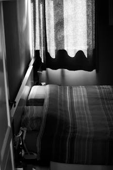 Monochrome photo of a cozy bedroom with draped curtains creating a calm atmosphere.