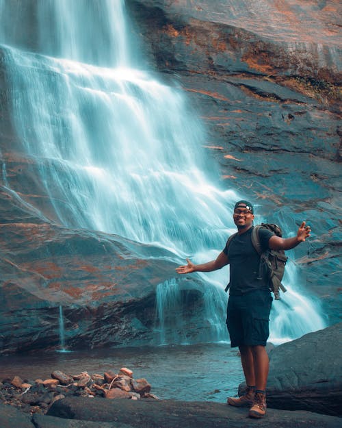 Man Standing on Rock in Front of Waterfalls