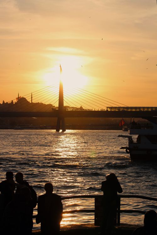 Free Dramatic sunset over Istanbul's suspension bridge with silhouetted figures by the water. Stock Photo