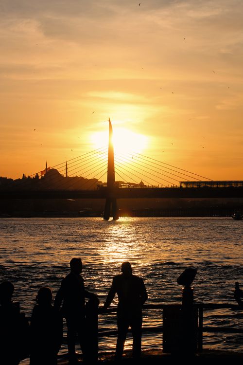 Free People silhouetted at sunset over Istanbul's iconic Golden Horn Bridge, reflecting urban serenity. Stock Photo