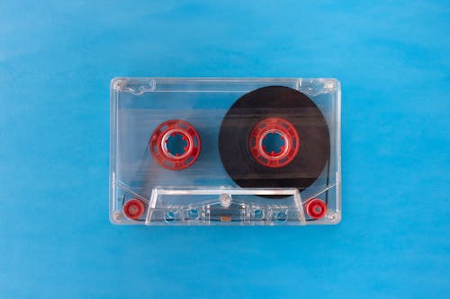 One transparent compact audio cassette with visible tape and red inner reels isolated on blue background. Top down view flat lay with empty space for text