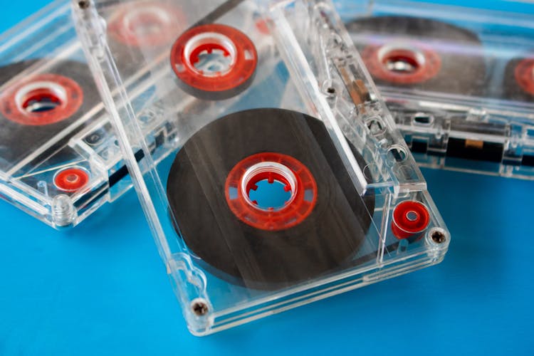 Several Transparent Compact Audio Cassettes With Visible Tape And Red Inner Reels Placed Randomly On A Blue Background. Selective Focus Technique