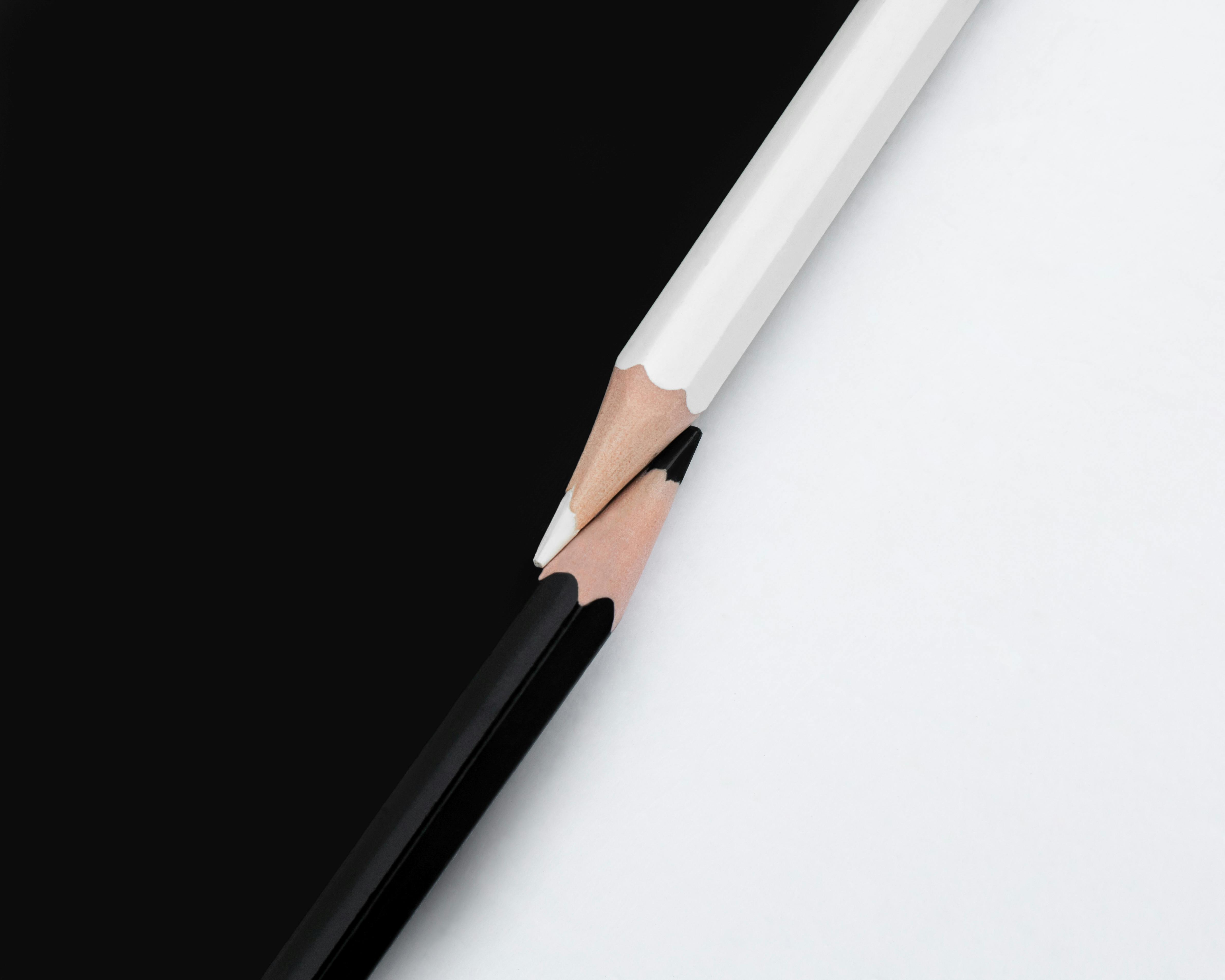 macro shot of two black and white colored pencils with the tips touching on a matching background with opposite colors top down view flat lay concept of contrast or opposites attract