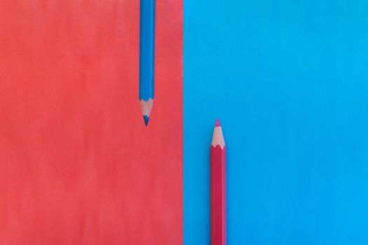 Pink and blue background divided vertically with two matching colored pencils placed on opposite colors. Top down view flat lay with empty space for text