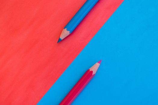 Pink and blue background divided diagonally with two matching colored pencils placed on opposite colors. Top down view flat lay with empty space for text