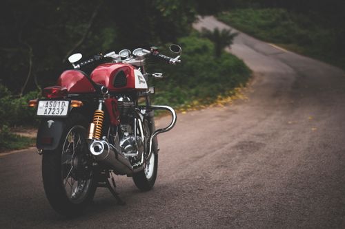 Free Classic red vintage motorcycle parked on a winding road surrounded by lush greenery. Stock Photo