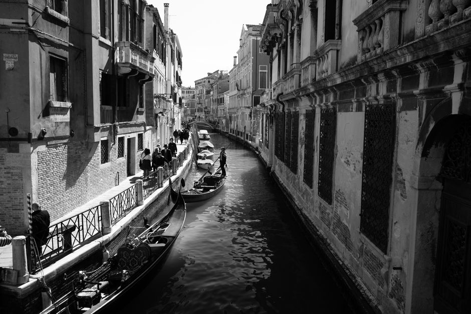 Black and white image of a Venetian canal with gondolas and historic buildings.