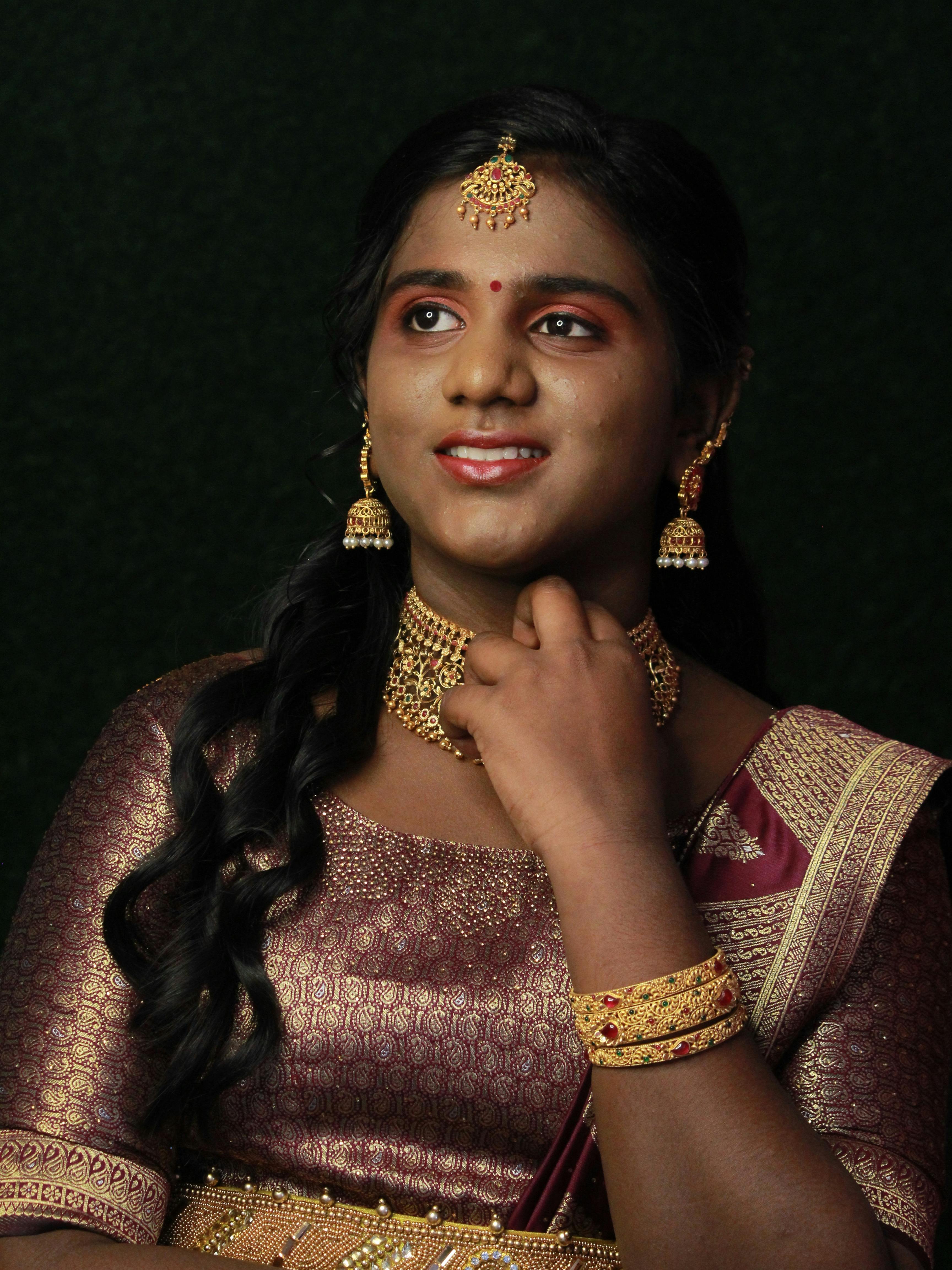 Woman adorned in traditional Indian attire with jewelry, smiling gracefully.