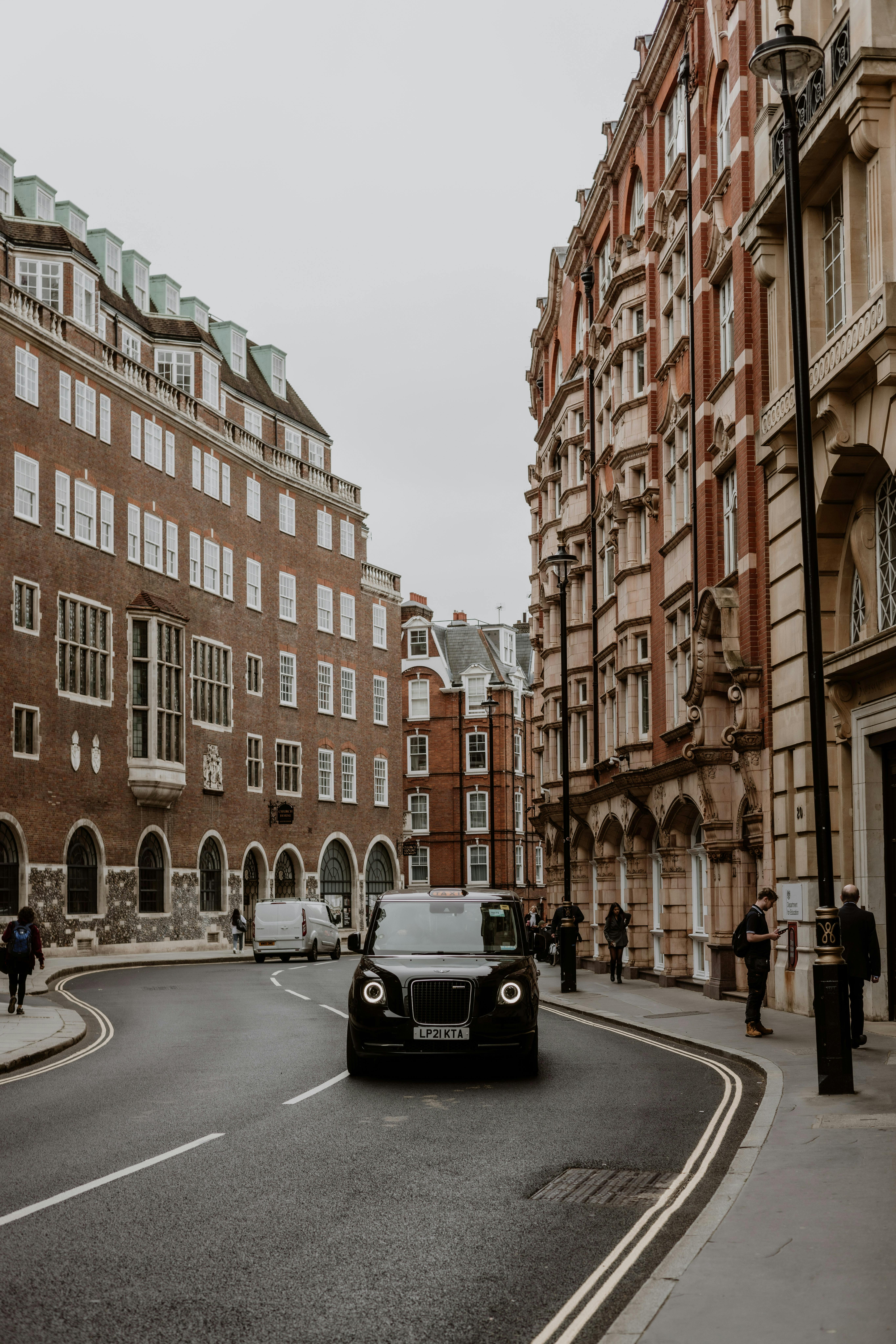 A black car navigates a historic winding street in London, showcasing urban architecture.