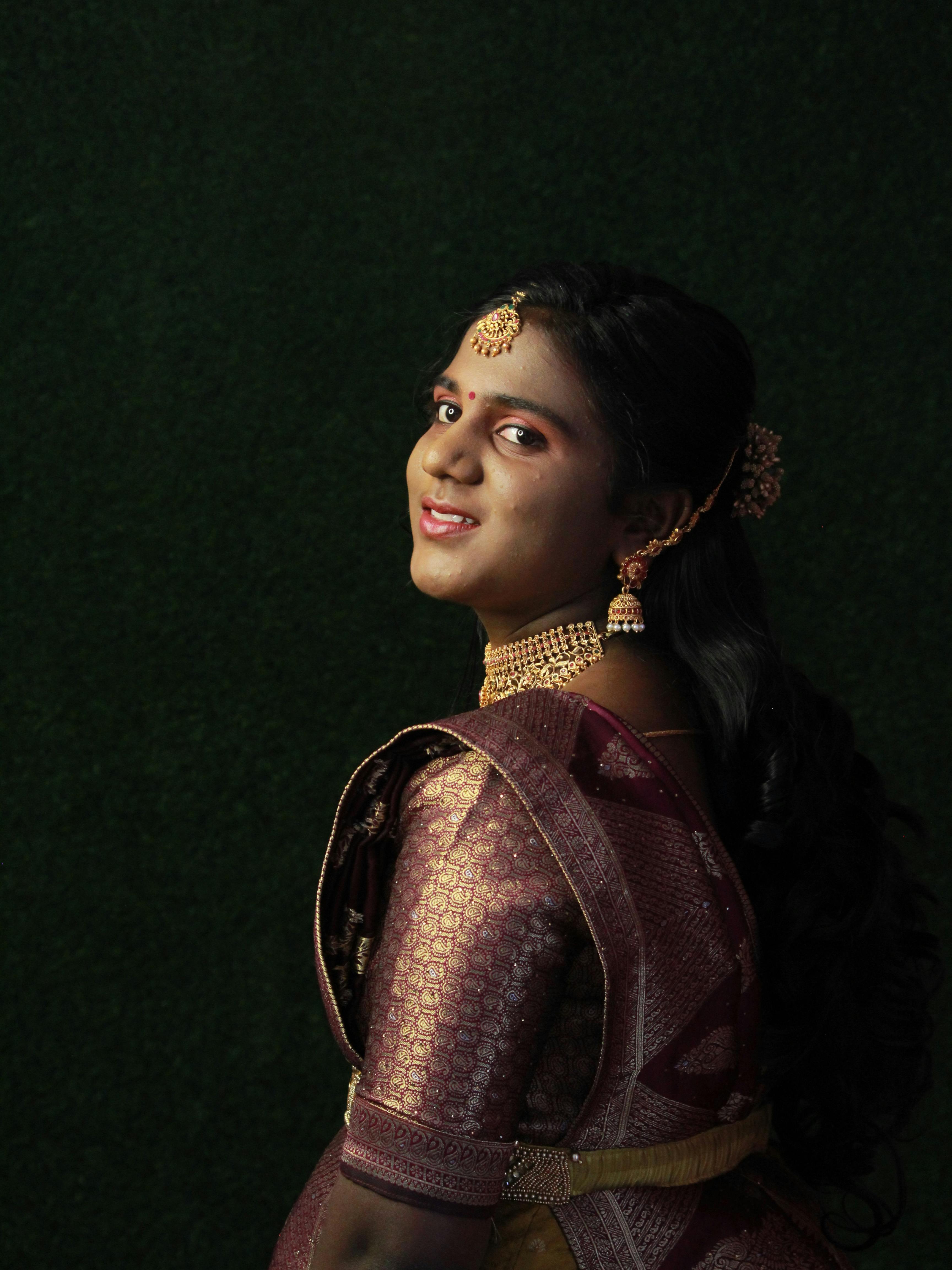 Portrait of a woman in traditional Indian dress with intricate jewelry against a dark backdrop.