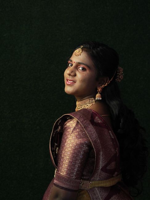 Portrait of a woman in traditional Indian dress with intricate jewelry against a dark backdrop.