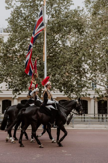 British cavalry riding horses in ceremonial uniform in a London parade beneath Union Flags.