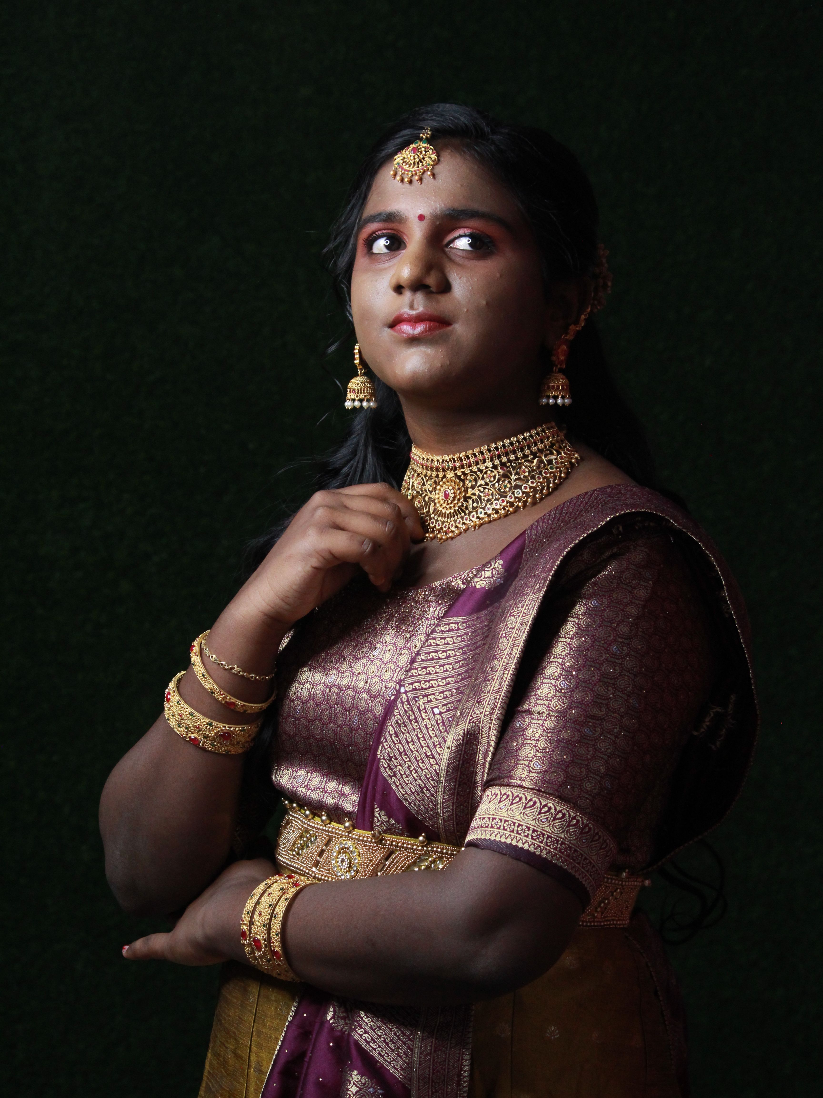 Portrait of an Indian woman in traditional attire with elegant jewelry against a dark background.