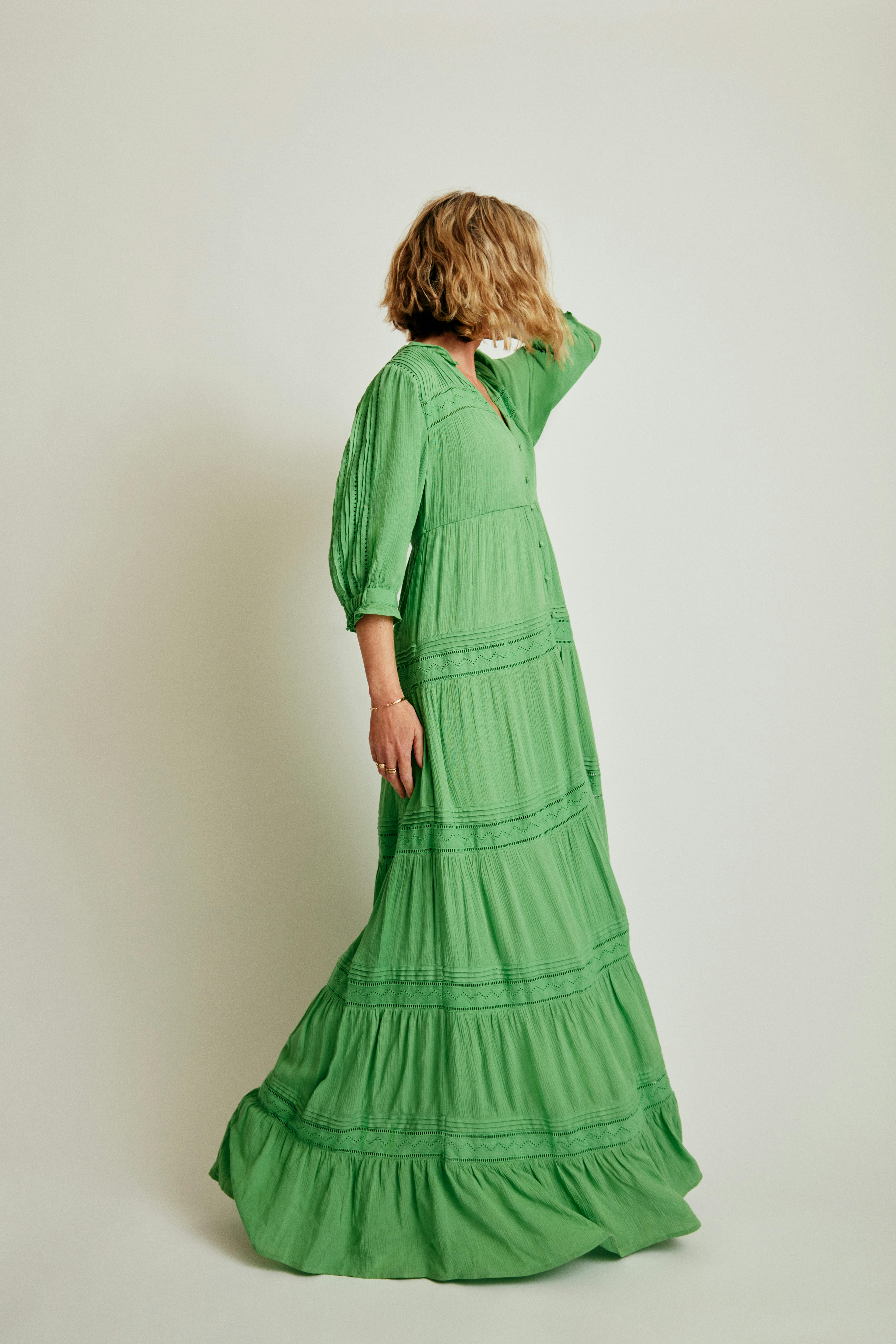 Elegant woman posing in a long green dress against a white background.