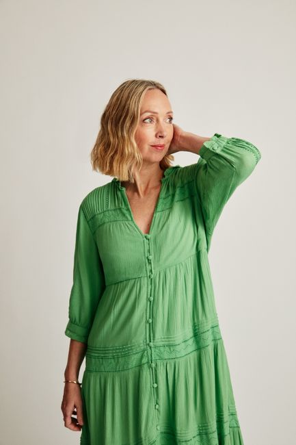 Blonde woman in green dress posing against a white background in a studio setting.