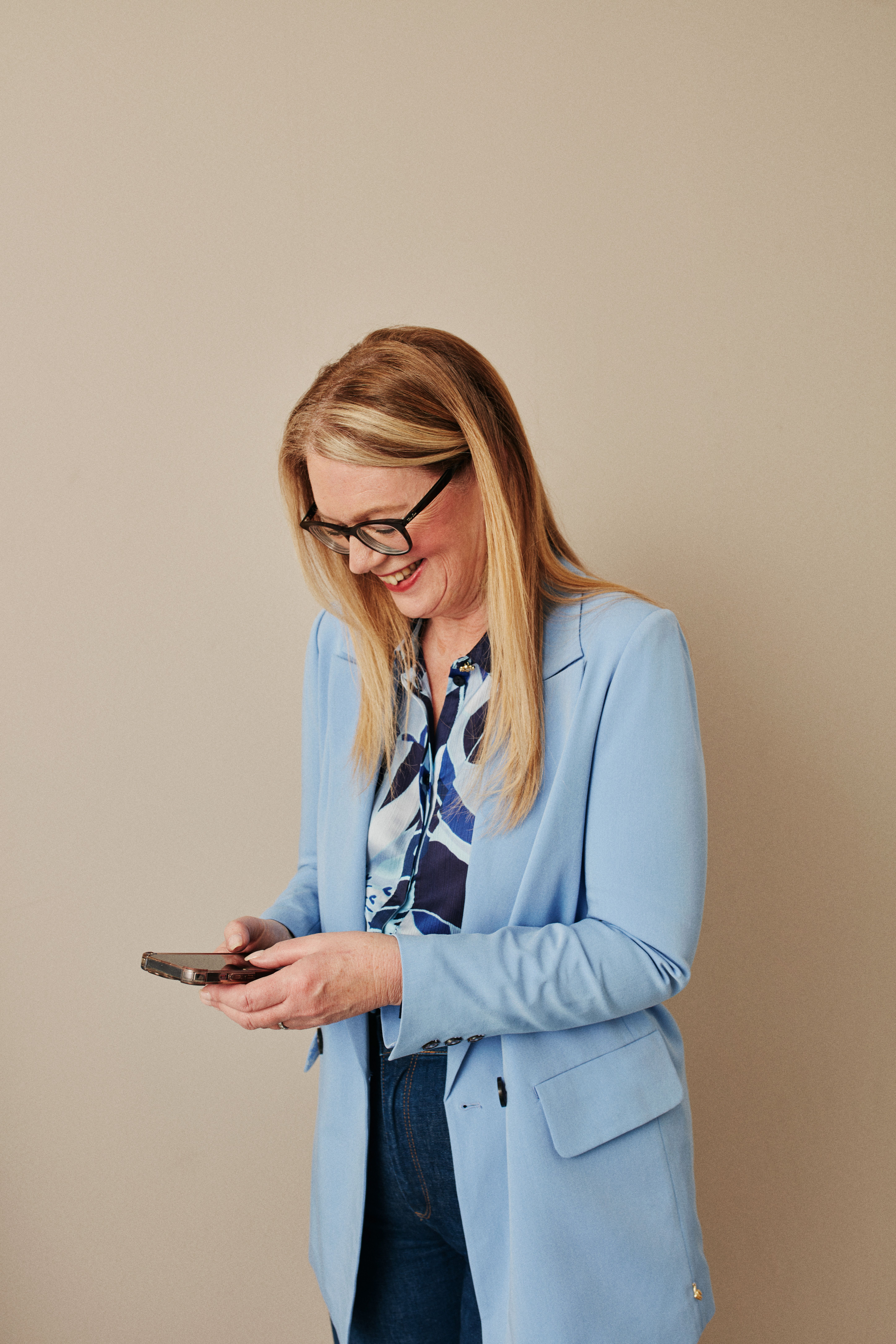 Businesswoman in blue blazer using smartphone against neutral background.
