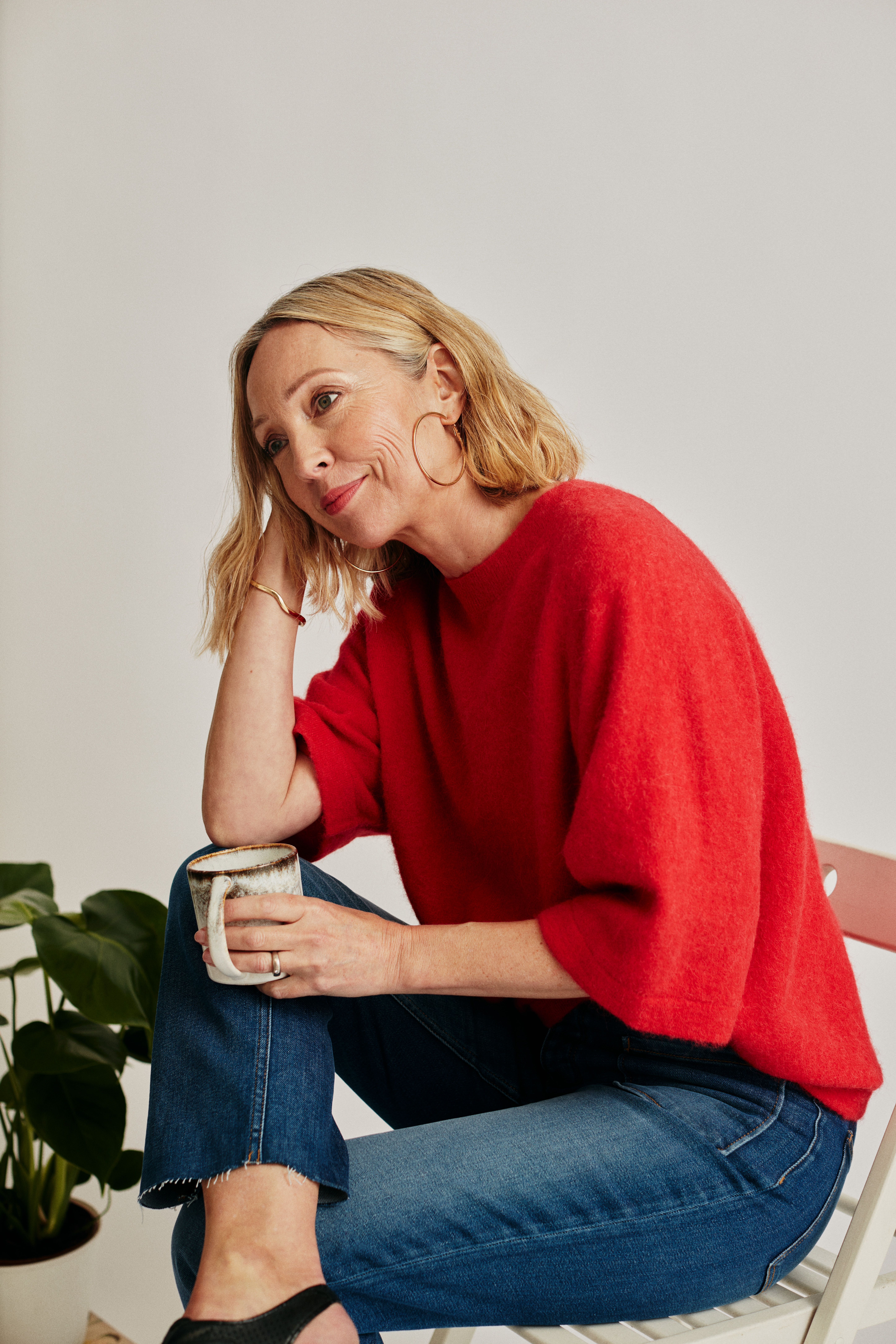 Woman sitting with a mug, wearing a red sweater in a studio setting.