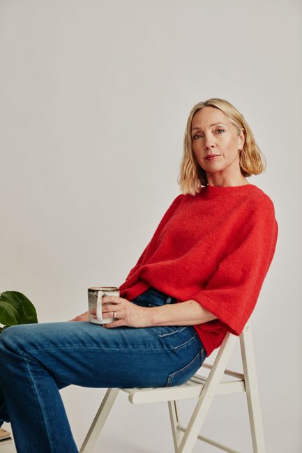 Stylish woman seated with mug in studio setting, displaying elegance and casual fashion.