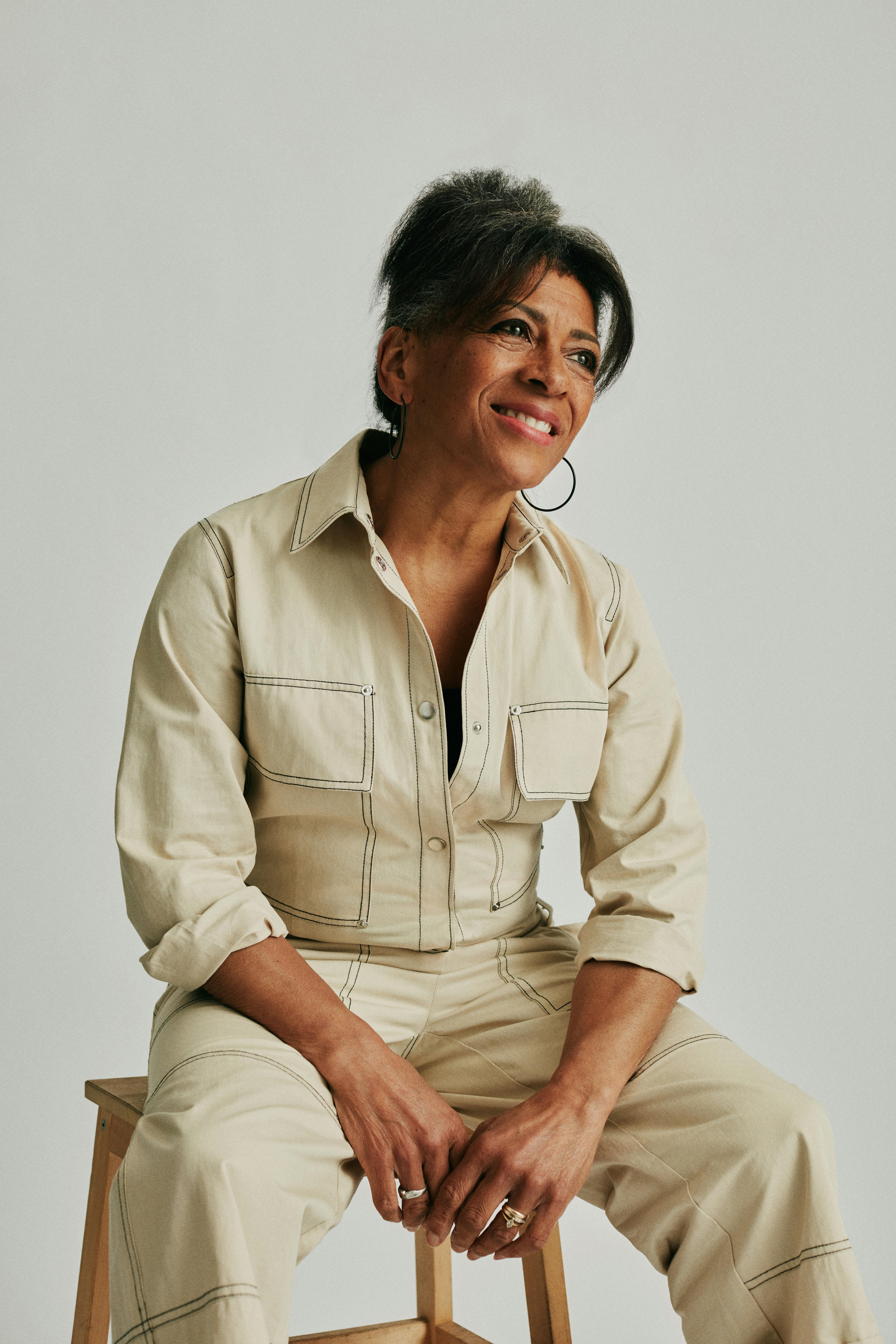 Smiling woman sitting elegantly in a studio wearing a beige jumpsuit with casual style.