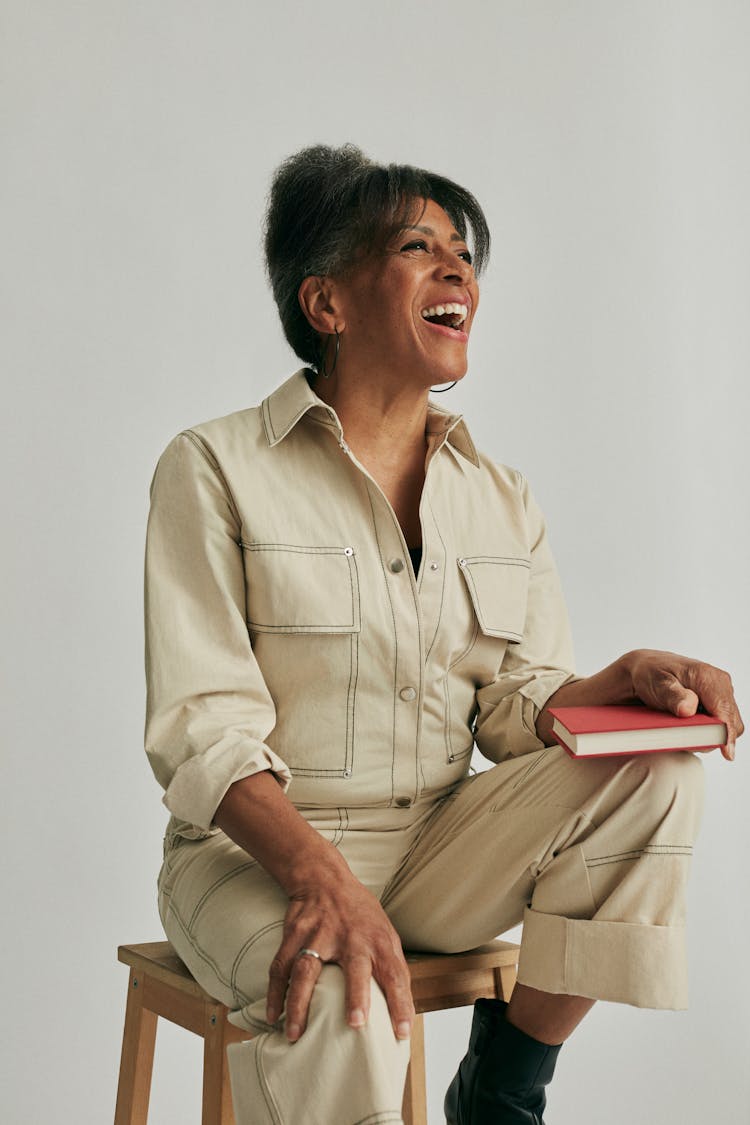 Laughing Woman Posing On Chair With Book On Knee