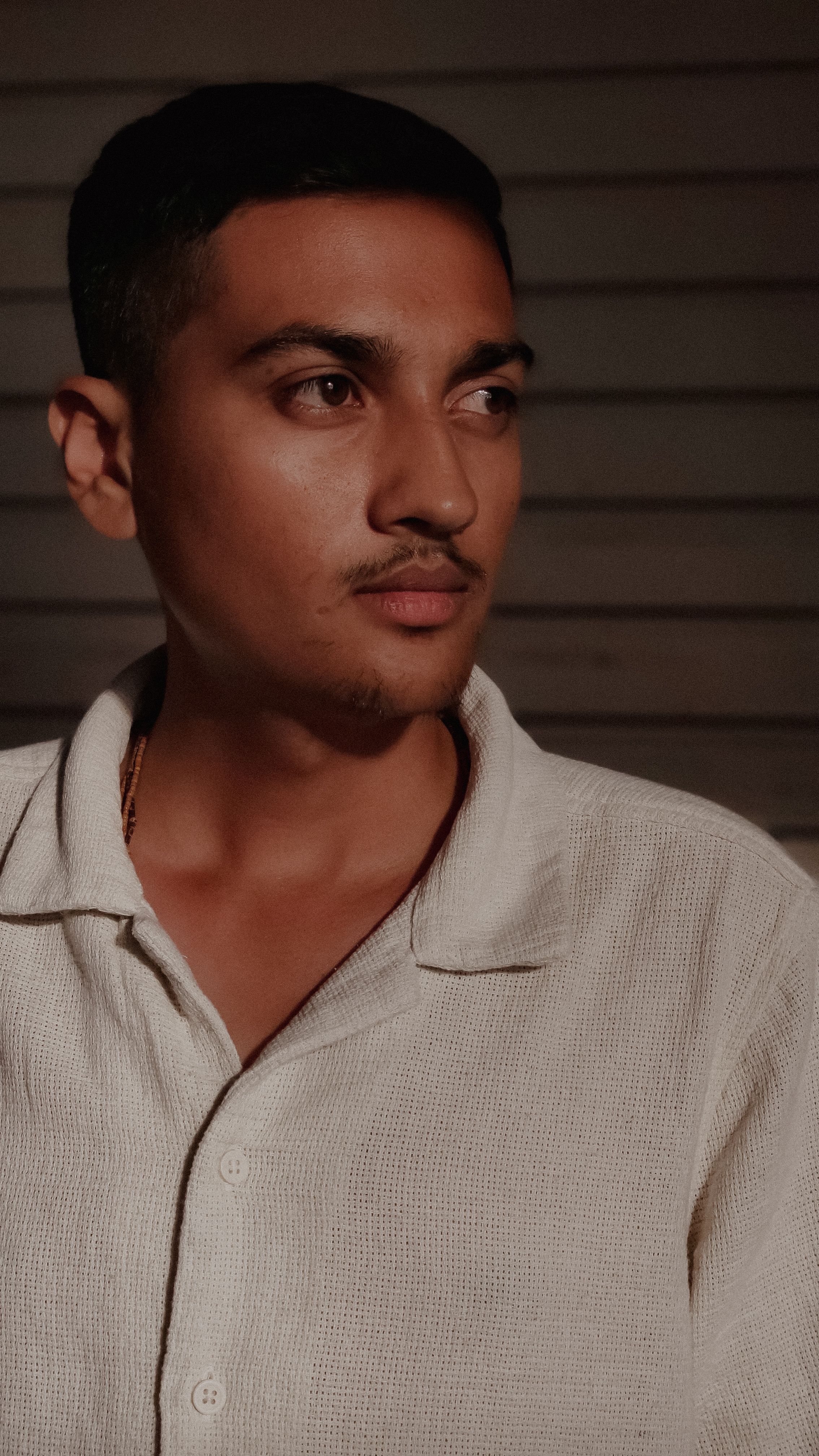 Portrait of a young South Asian man wearing a white shirt, looking thoughtful indoors.