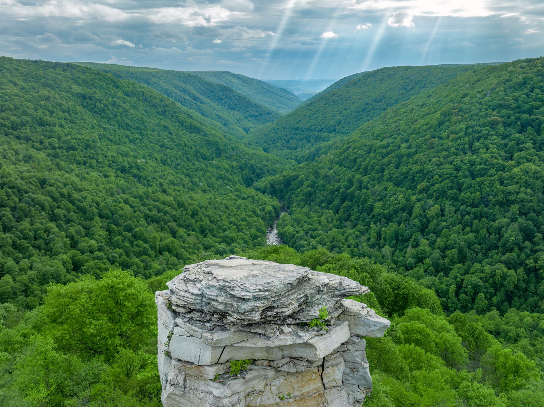 Breathtaking aerial view of a lush green valley in West Virginia, under dramatic sun rays.