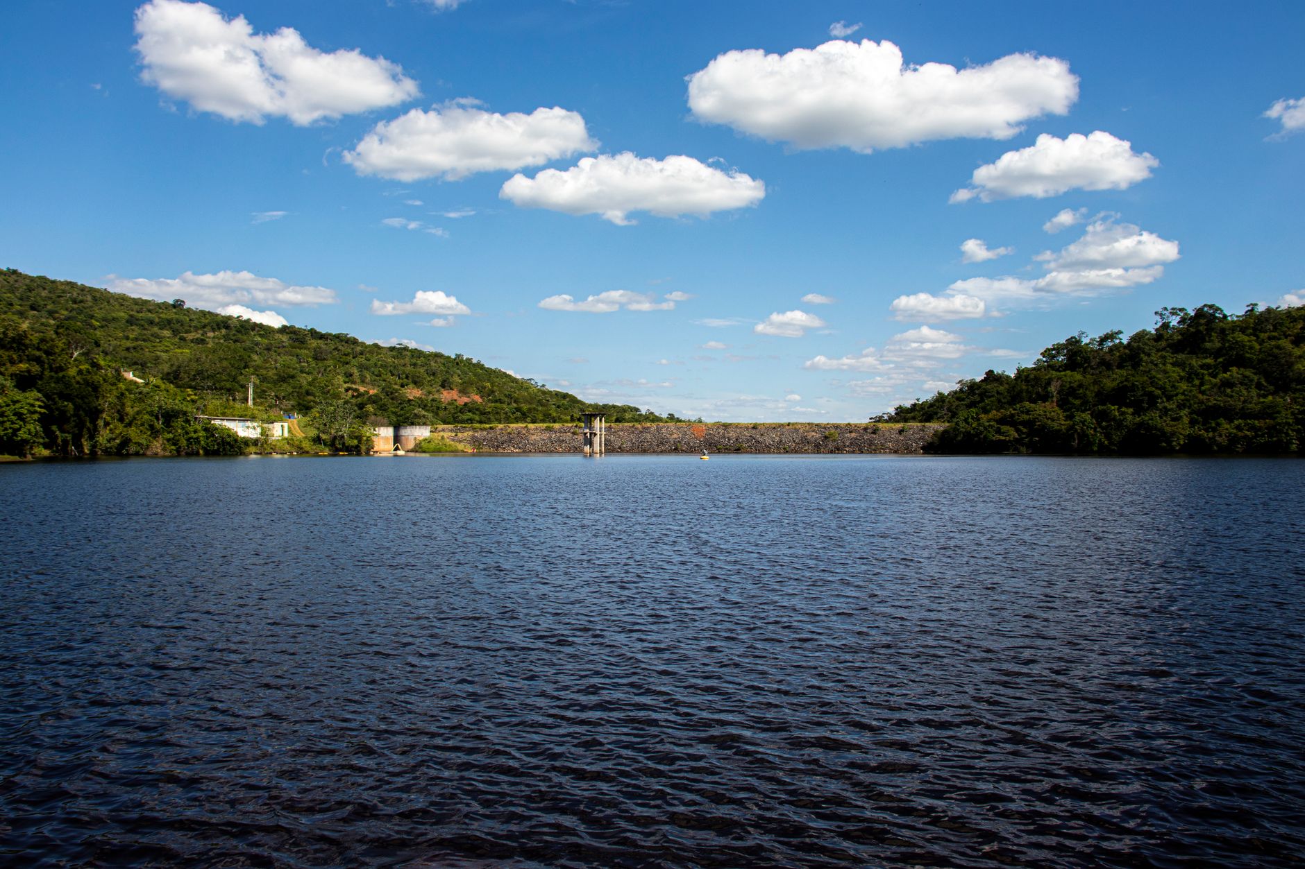Peaceful summer landscape with blue sky, lake, and wooded hills.