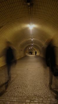 Long exposure captures people walking through a lit underground tunnel.