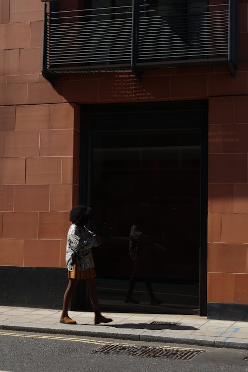  A Woman Walking on the Sidewalk in front of a Building in City 