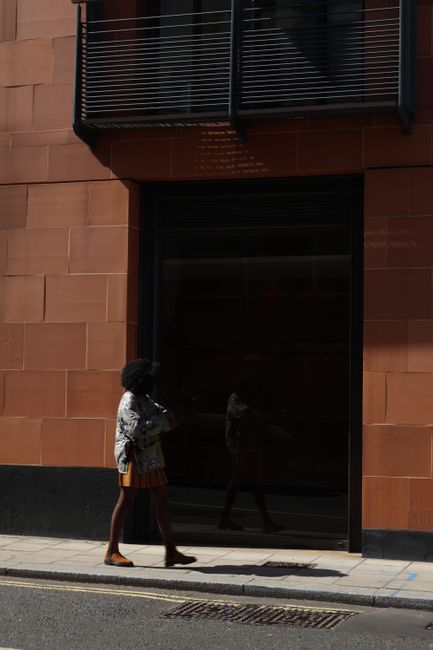 A woman walks past a modern building in London, England on a sunny day.