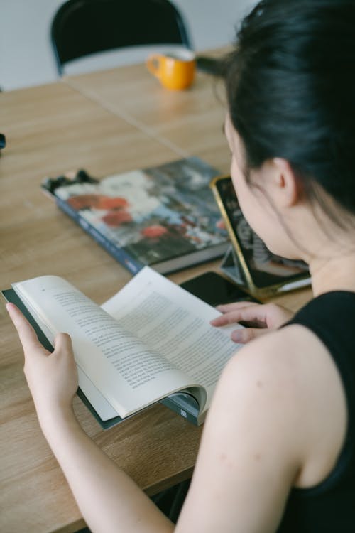 Young Woman Sitting at the Table and Reading a Book 