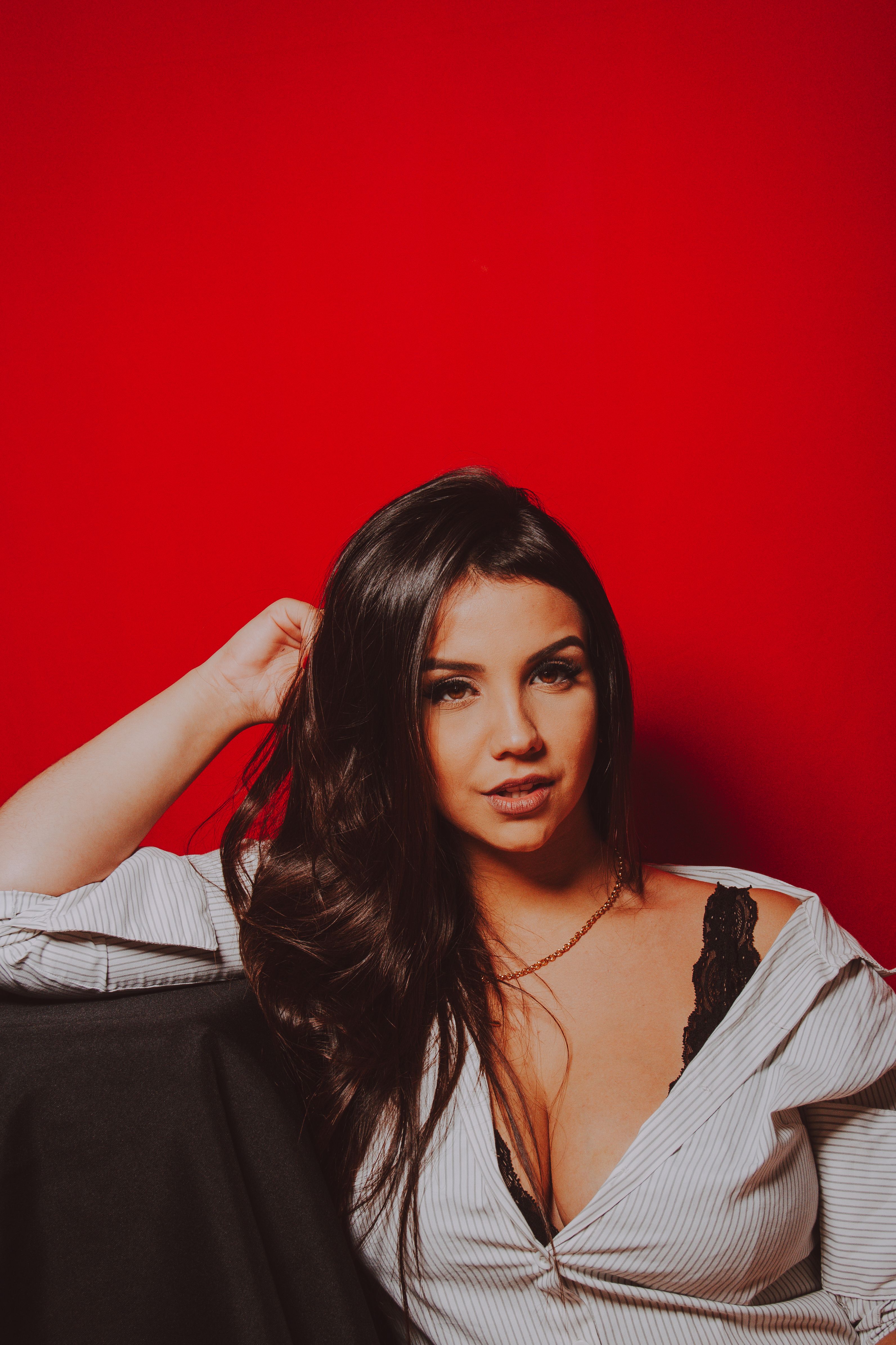 Striking portrait of a young woman in a casual pose against a vivid red background, highlighting her features.