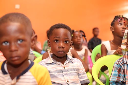 A group of children seated in a colorful classroom setting, focusing attentively.