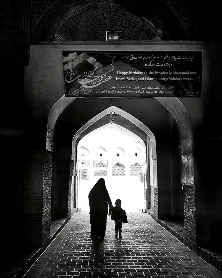 Mother Walking With Child In Alley In Town In Black And White