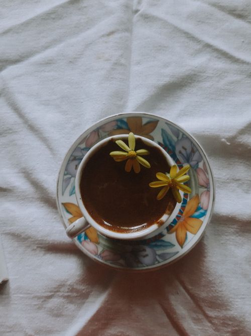 Free A floral-patterned coffee cup and saucer with yellow flowers, beautifully presented on a white tablecloth. Stock Photo