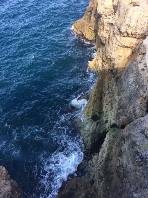 Free Stunning view of a steep rocky cliff with blue ocean waves crashing below. Stock Photo