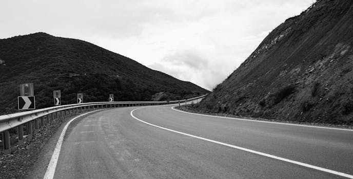A scenic curved mountain road captured in black and white, offering a tranquil outdoor view.