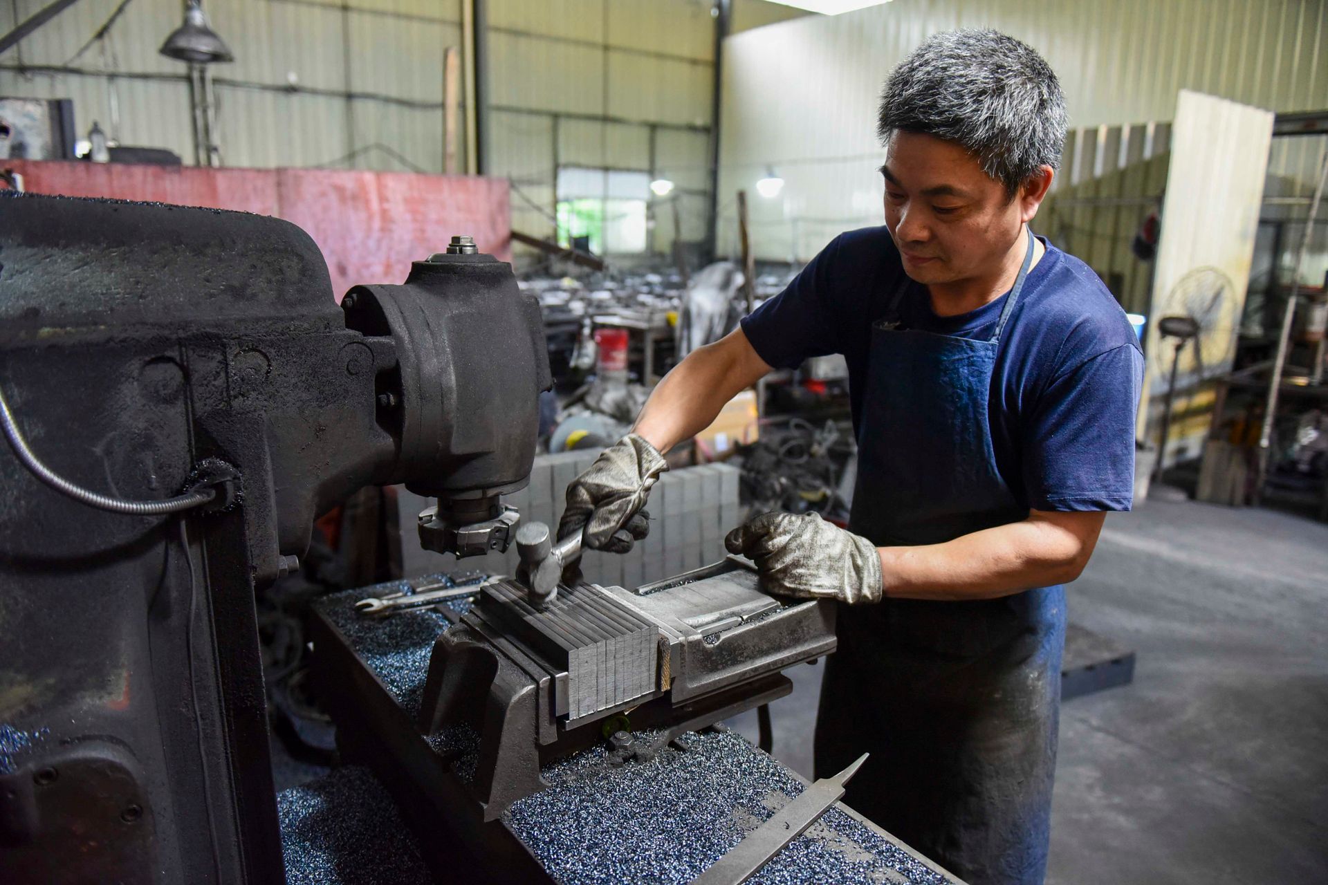 Asian man working in an industrial workshop, operating machinery with focus and precision.