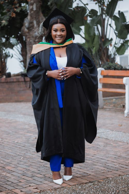 Free Female graduate smiling in cap and gown, celebrating academic achievement outdoors. Stock Photo