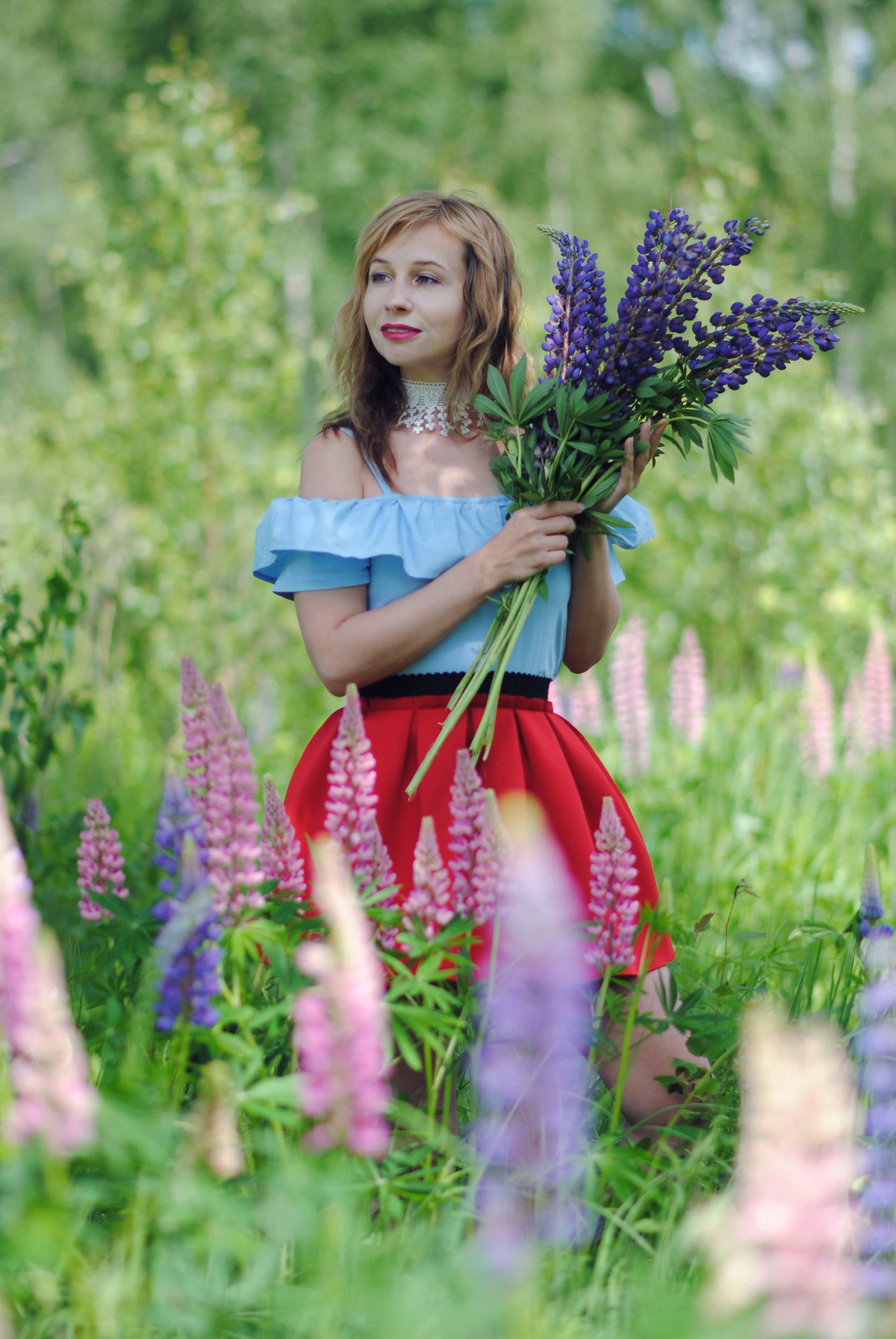 Young woman enjoying a sunny day in a flowery meadow, holding purple lupins.