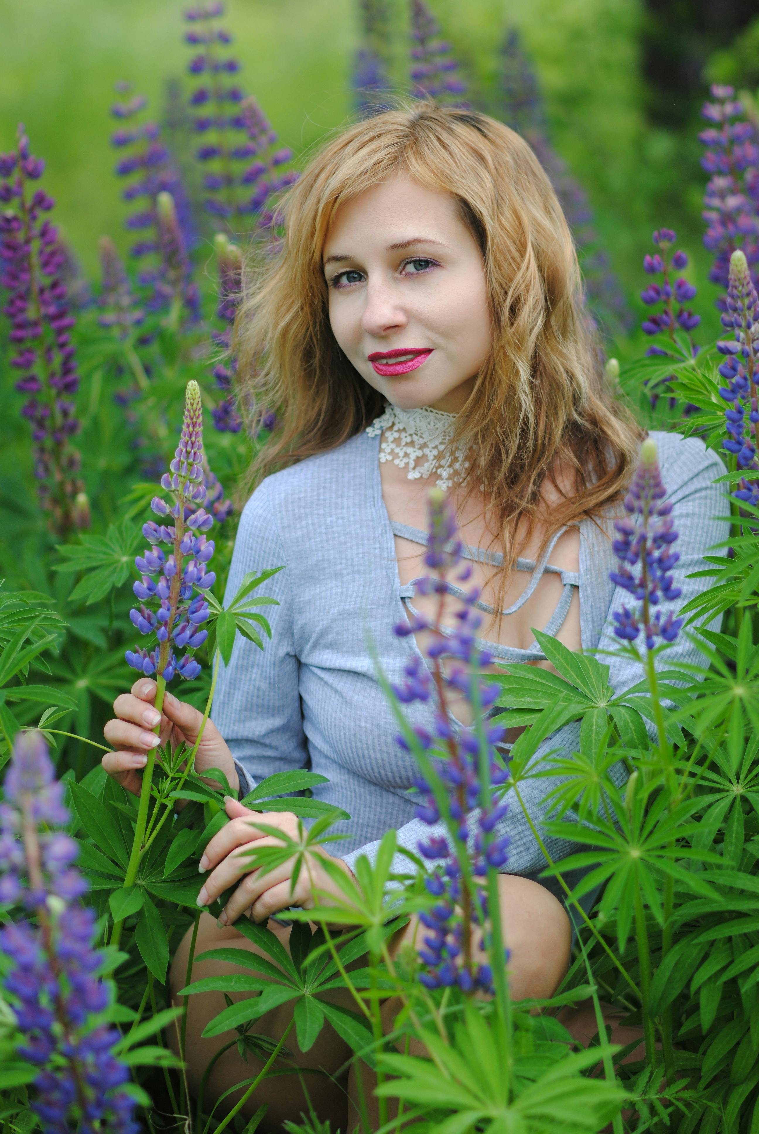 Charming redhead woman surrounded by purple lupines in a lush outdoor setting.