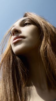 Artistic low-angle shot of young woman looking upwards, accentuating her facial features against a clear sky.