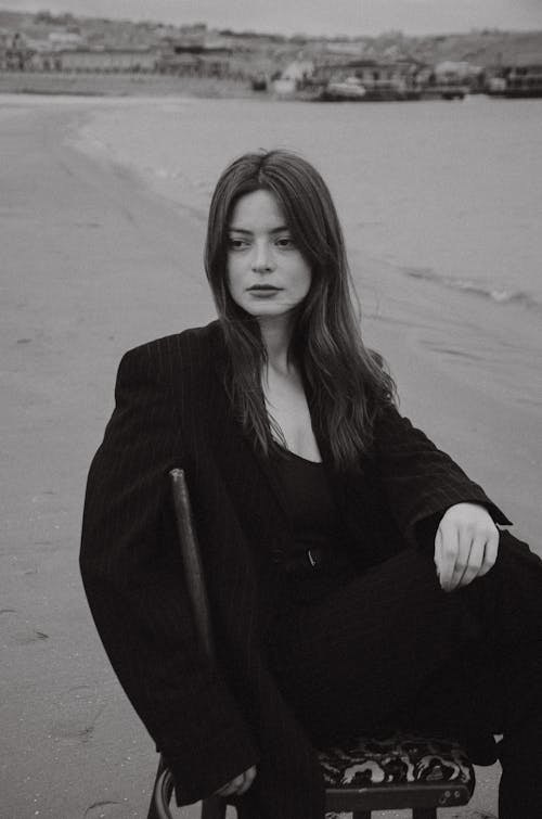 Woman in Suit Sitting on Sea Shore in Black and White