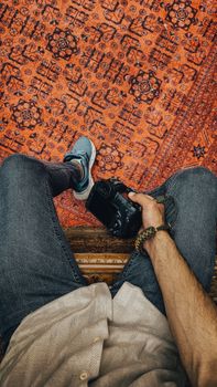 Overhead view of a person with a camera, showing jeans and ornate carpet.
