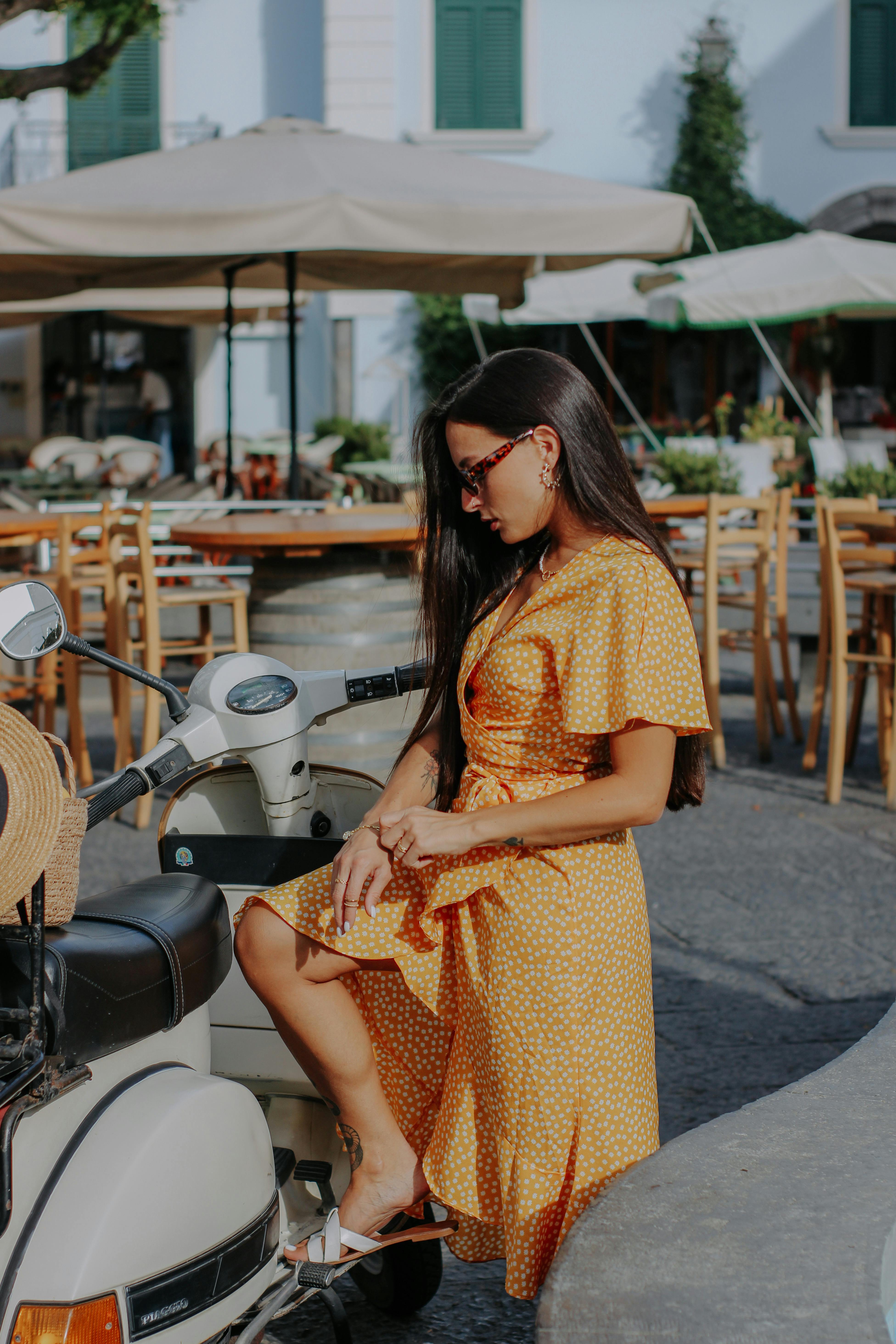 Free Chic woman in yellow dress relaxing by scooter in summer urban setting. Stock Photo